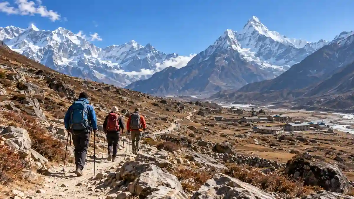 Three trekkers with backpacks walking along a rocky Himalayan trail with snow-covered mountains and stone buildings.