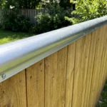 A metal coyote roller bar installed on top of a backyard wooden privacy fence for pet protection.